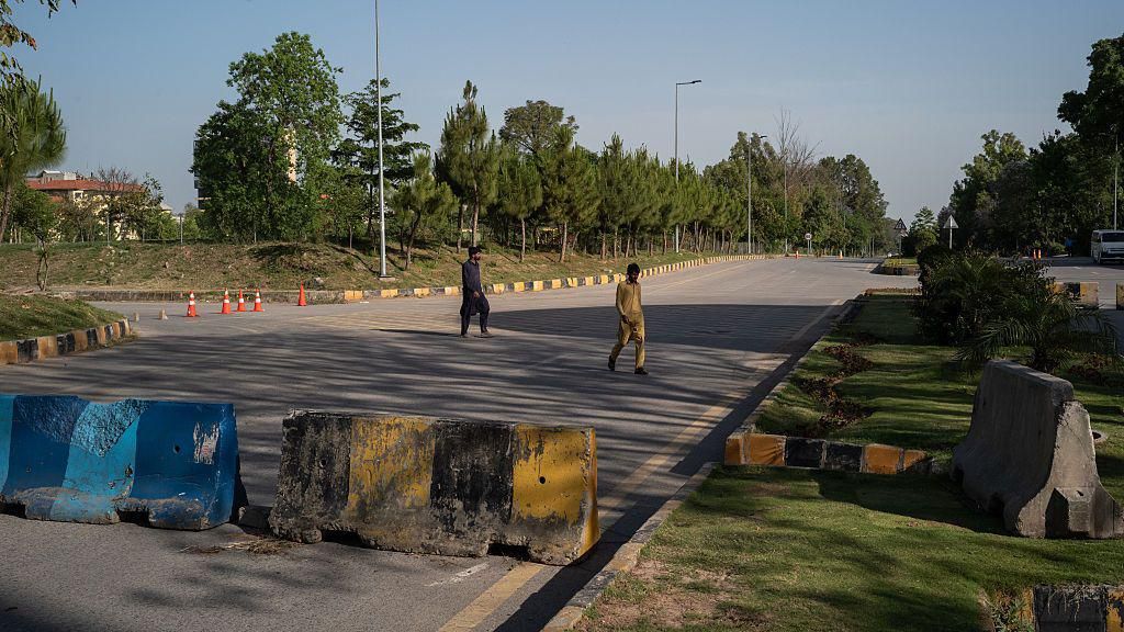 Two people crossing a road which has been blocked off with concrete barriers