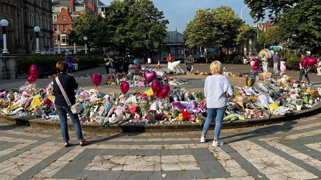 people look at balloons and flowers at Southport tribute site