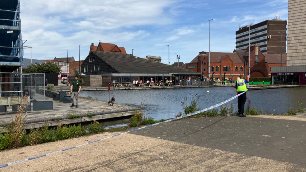 A police officer ties a line of police tape along the edge of the canal in Walsall