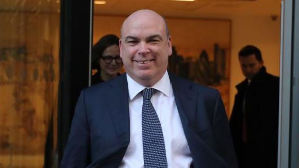 Mick Lynch smiles wearing a suit as he leaves a building