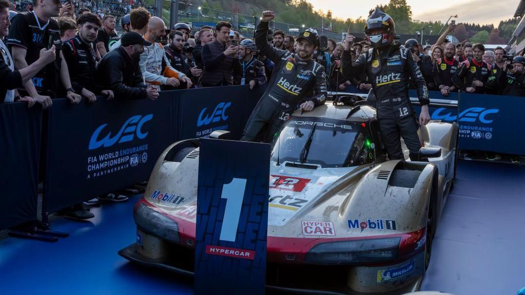 Drivers William Stevens and Callum Ilott celebrate winning the 6 Hours of Spa race by posing in front of the first place sign in their Jota Porsche 963 hypercar