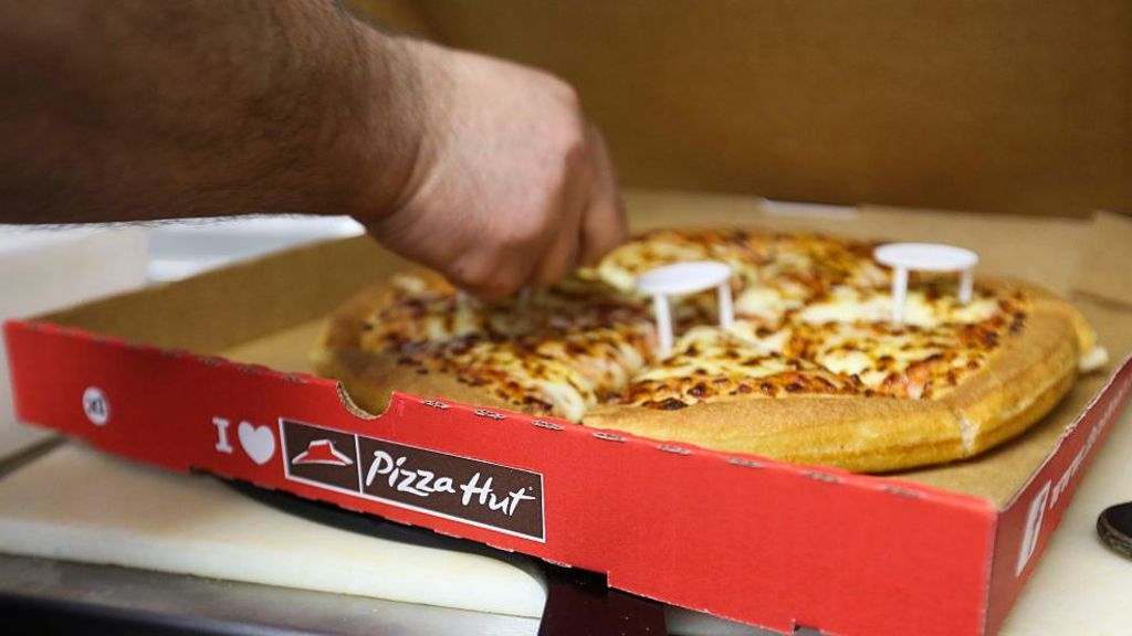 A person reaches into a pizza box and cuts a pizza