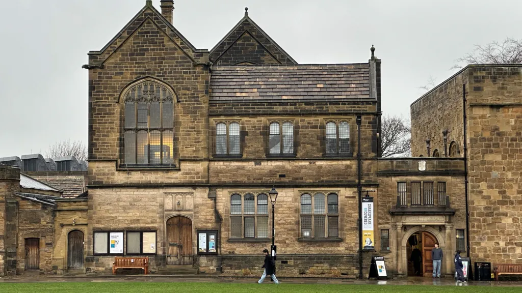 The Palace green Library. It is an ornate and historical looking building with large arch windows next to a green.