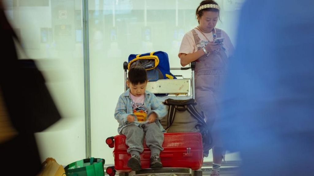 A child and adult shown checking their phones as people pass by during the outage in Thailand on 19 July