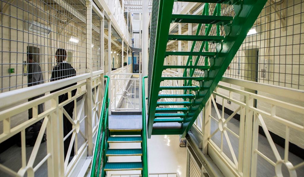 The stairs and corridor of HMP Portland in Dorset are pictured in 2014, with an unidentifiable police officer escorting a prisoner into their cell to the left of frame. 