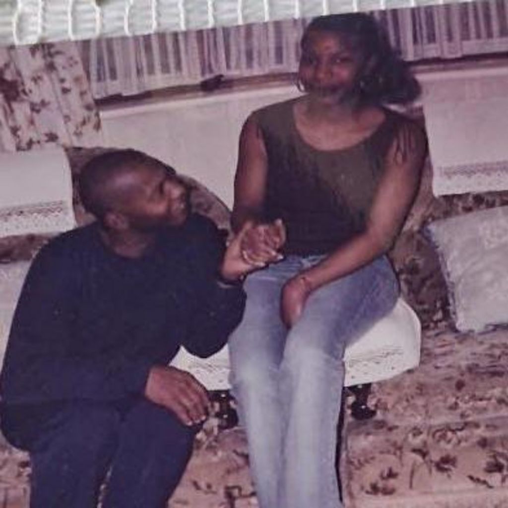 An old photo of Basil sitting beside his daughter Naomi, holding her hand and smiling at her, as she looks towards the camera and smiles. They appear to be in a front room, with her seated on a white sofa   