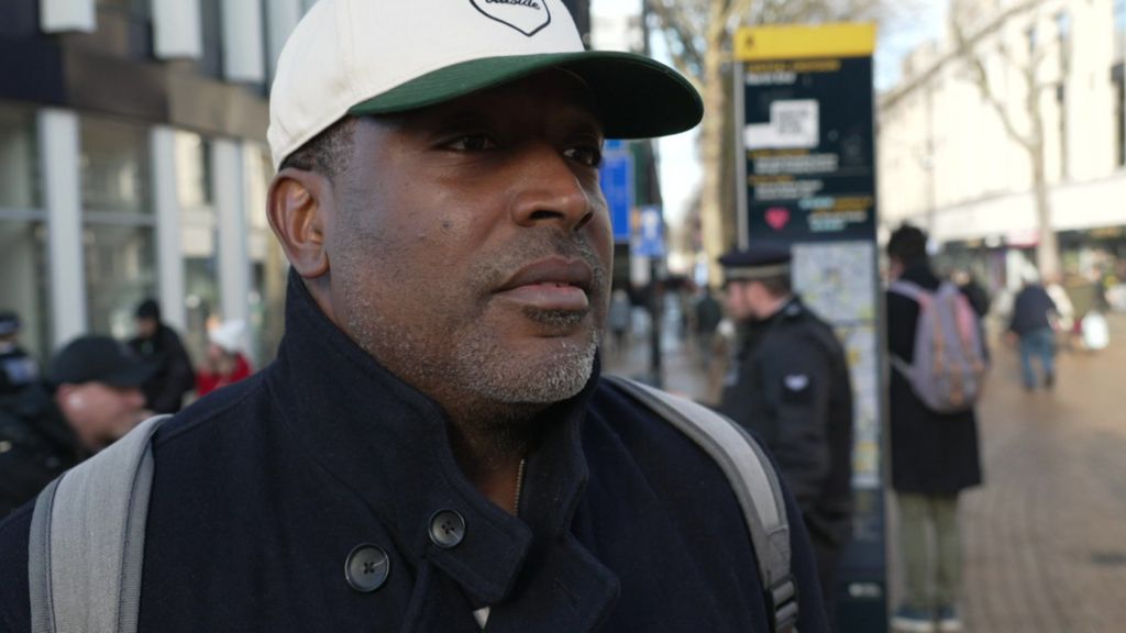 Lance Payne, wearing a baseball cap, stands on a busy Croydon high street