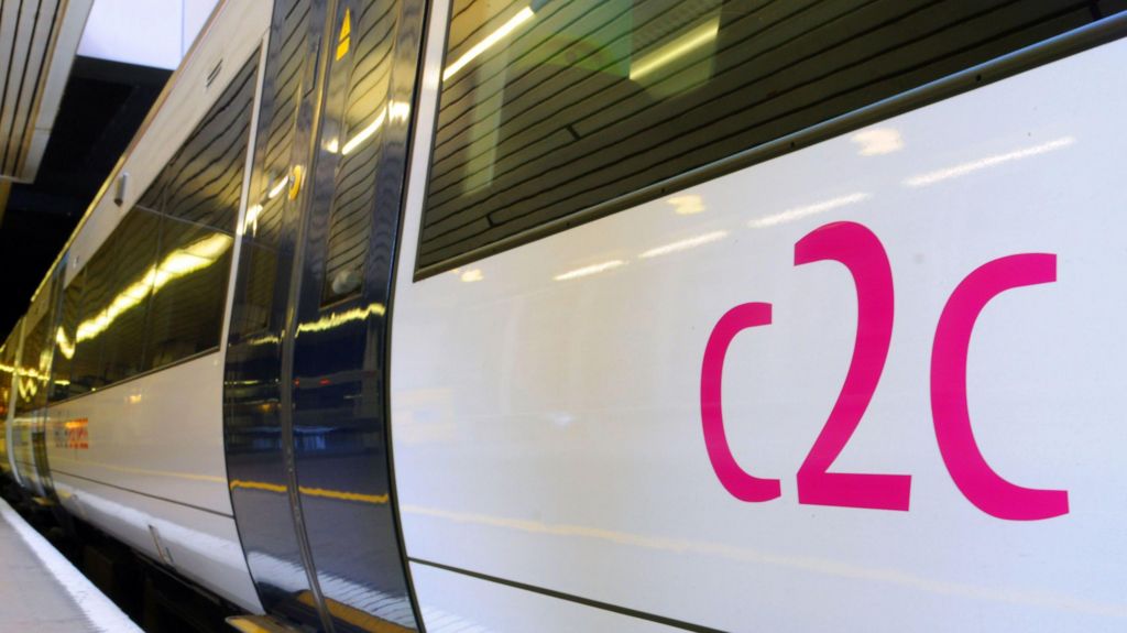 A white train with c2c printed on the side in pink. The train is parked next to a platform.