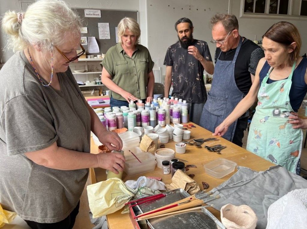 People taking part in a workshop. Three women and two men stand around a table with craft materials on it.