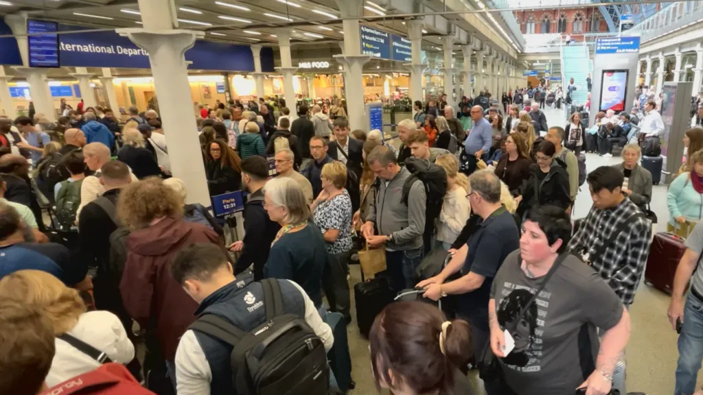 A crowd of people at London St Pancras station in London. They're carrying rucksacks or suitcases as they wait to go through departures and board a Eurostar train across the Channel.