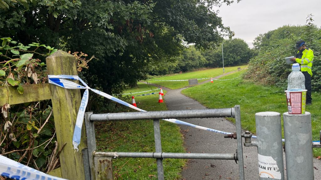 Police tape on a gate into a park with an officer in the background