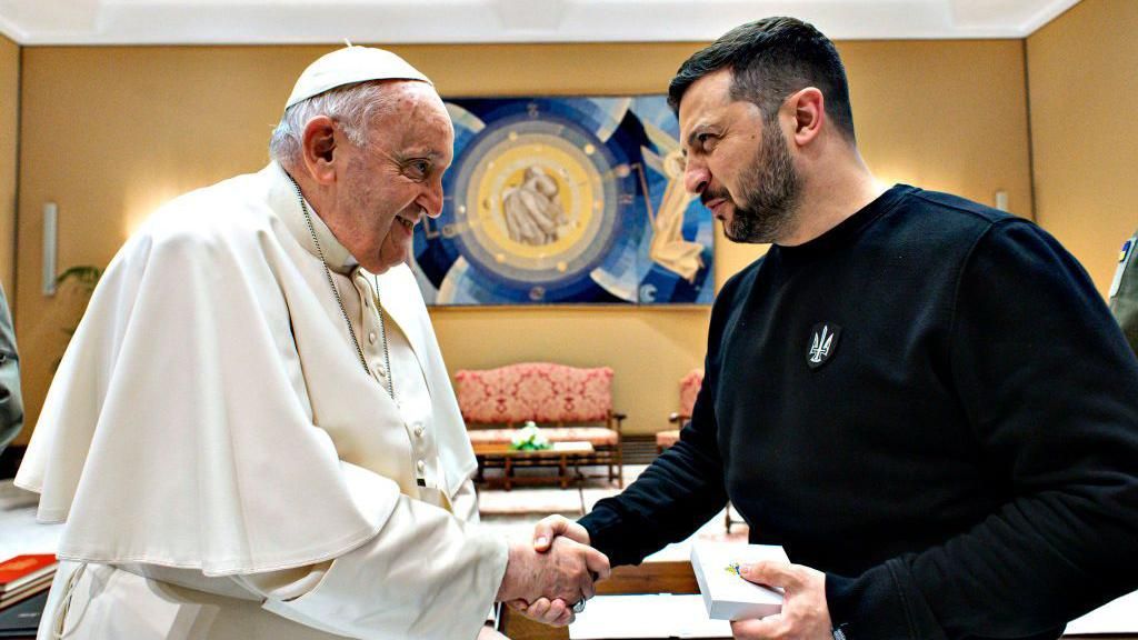 Pope Francis meets with Ukrainian President Volodymyr Zelensky. They are shaking hands and looking at each other.