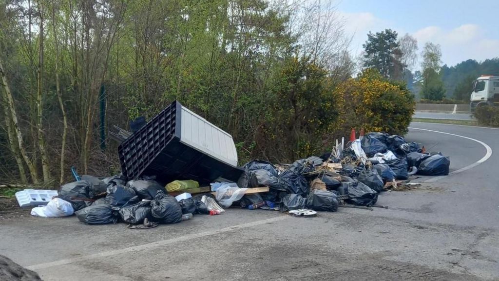 dozens of bin bags filled with rubbish in a pile at the side of the road