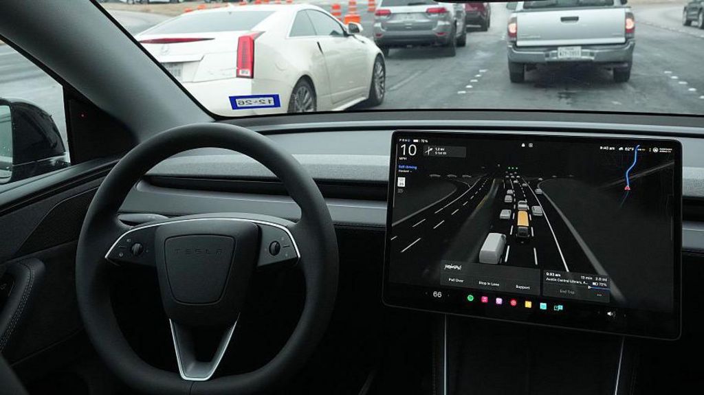 A black steering wheel and large screen to the right which shows lanes of traffic and vehicles in it.