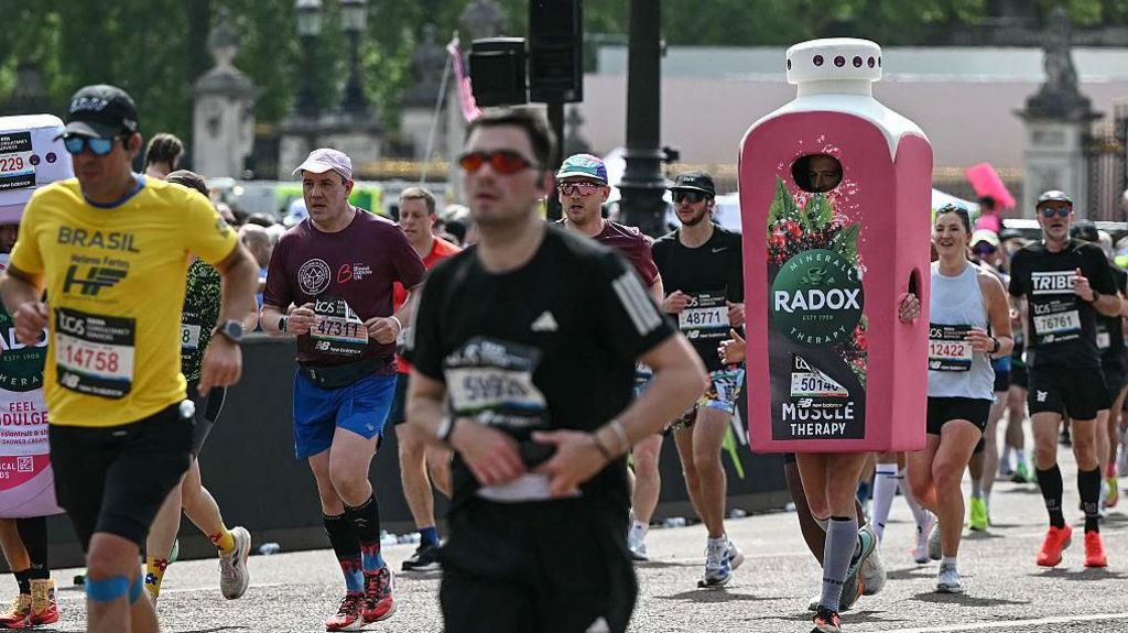 A marathon participant runs amongst the crowd while wearing a large, pink costume shaped like a Radox "Muscle Therapy" shower gel bottle.