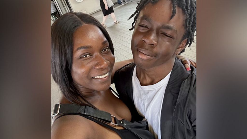 Jodian and Daejaun pose closely for a selfie in an indoor public space with tiled flooring, while other people walk in the background near wall‑mounted clocks and signage.