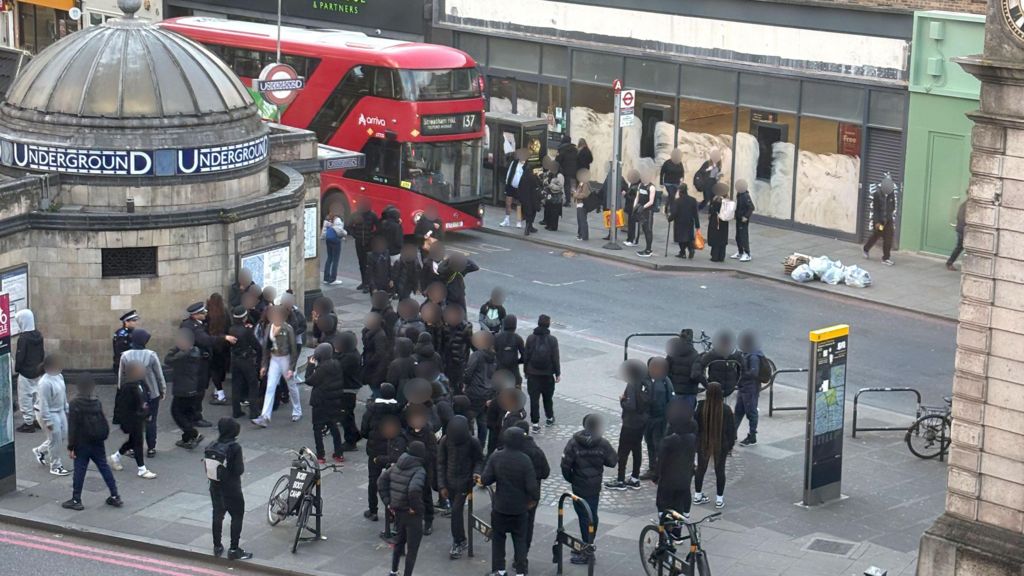 A group of people, mostly in black clothing, standing together on Clapham High Street.