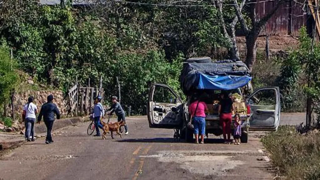 Street in Concordia, Mexico. A car and several people are in the foreground, with houses and trees on a gill in the background
