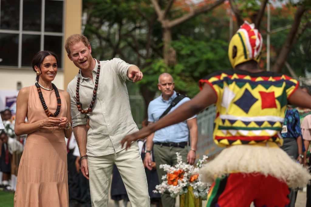 Prince Harry and Meghan watch a traditional Nigerian dancer performing outside the Lightway Academy in Abuja