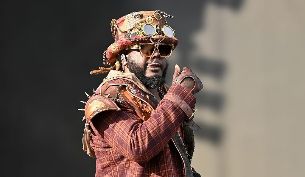 T-Pain wears a steampunk outfit, with a red checked pattern and a top hat, bedecked with sunglasses, stud and chains. 