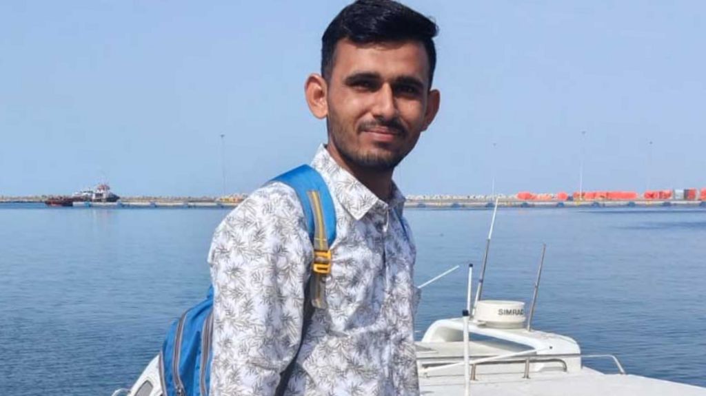 Sunil Puniya stands on the shore next to a boat in the left hand image. In the right hand image the Skylight is seen in the distance on fire with plumes of black smoke billowing into the sky.