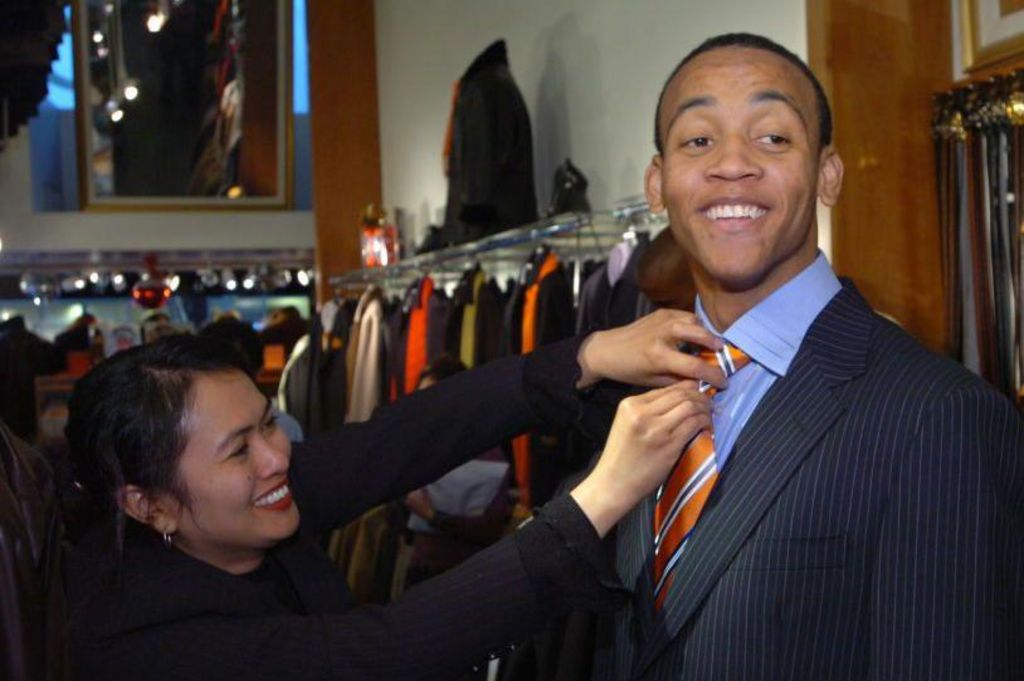 A shop clerk fixing the tie of basketball player Monta Ellis, wearing a suit, in 2005