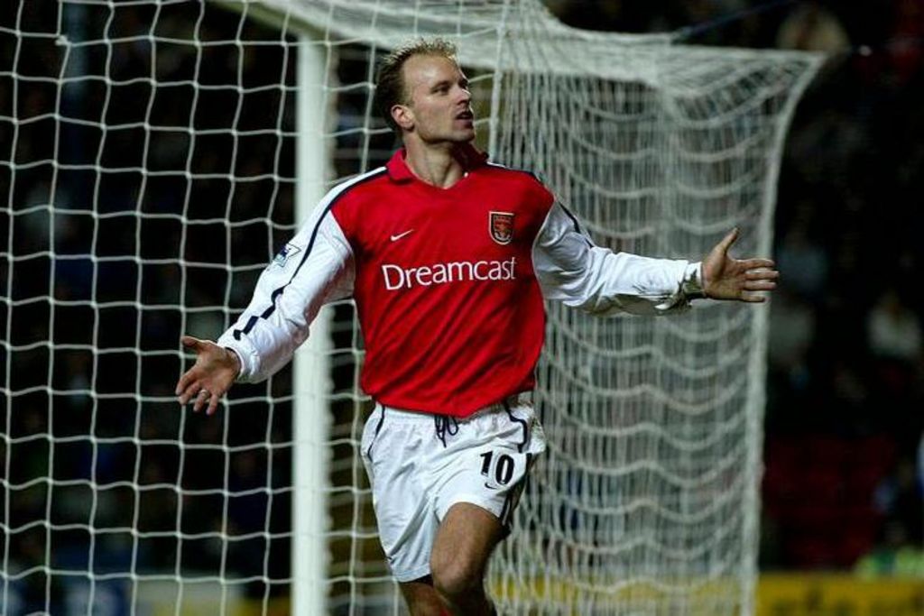 Dennis Bergkamp in a red Arsenal shirt celebrates a goal. His arms are outstretched in front of the net
