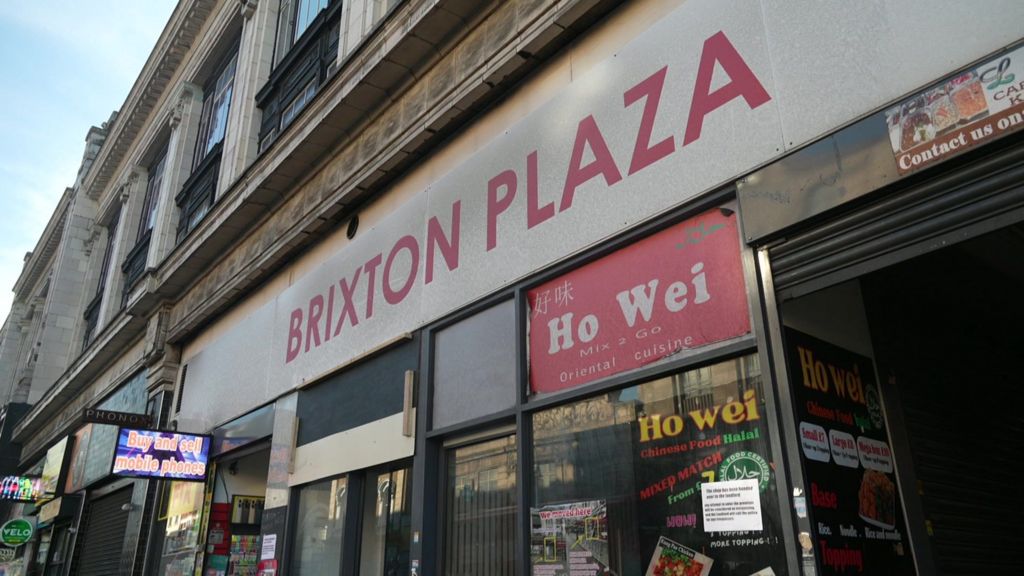 A old building with signage reading Brixton Plaza. Different advertising can also be seen around the building.