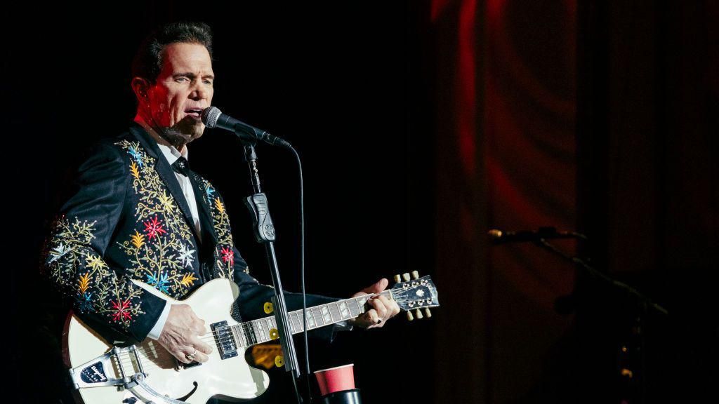 Chris Isaak on stage, playing a white Gibson guitar