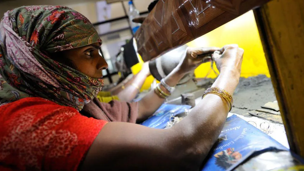 A woman wearing a red kurta and green stole with flower patterns wrapped around her face works in a jewellery shop in India's Jaipur city.