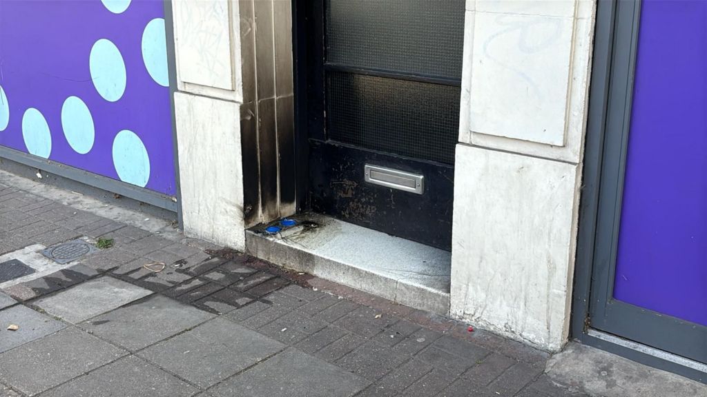 A building doorway showing scorch marks near the entrance and debris on the pavement