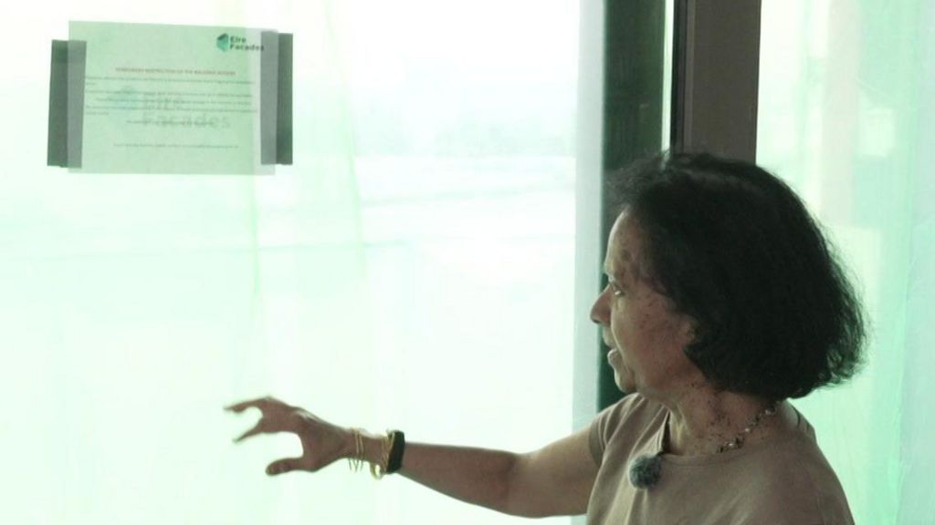Woman looks at thick green protective sheeting surrounding her balcony