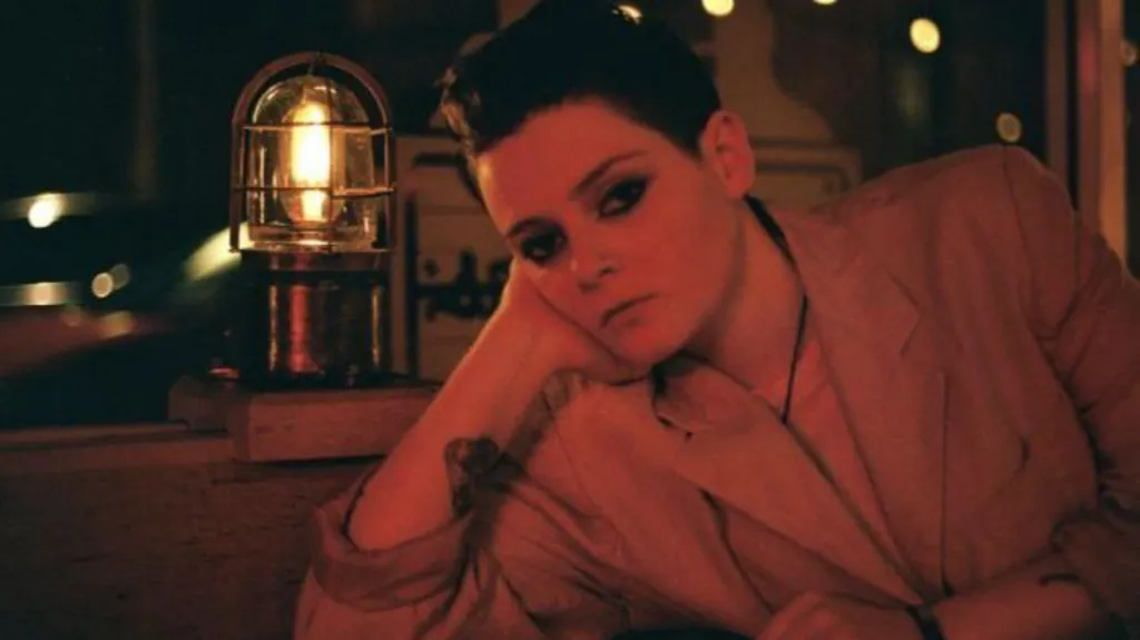 Susie Blue is sitting with a hand resting. A lantern is in the background. 