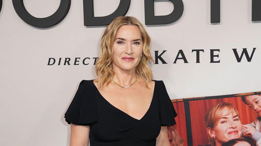 Kate Winslet smiles as she stands in front of a poster of her new film.