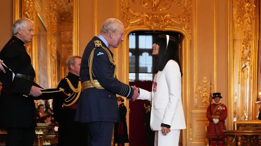 Claudia Winkleman shaking hands with King Charles III while being made an MBE at a ceremony at Windsor Castle
