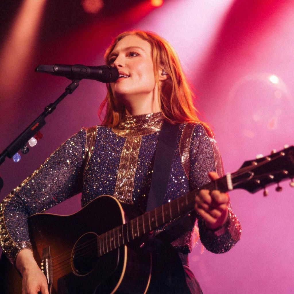 Freya Ridings plays at Hotel Café in New York. She is wearing a diamante purple haler-neck top and strumming an acoustic guitar
