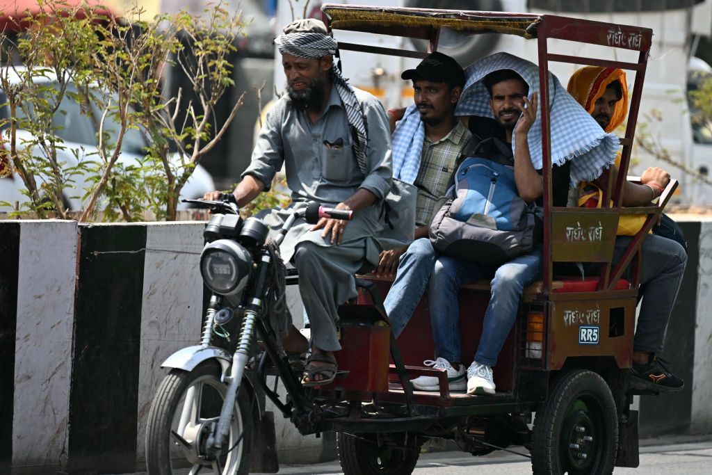 People travelling on an electric rickshaw cover their heads during a hot sunny day in old quarters of Delhi on May 21, 2024. Indian authorities in the capital have ordered schools shut early for the summer holiday, after temperatures hit 47.4 degrees Celsius (117 degrees Fahrenheit) with Delhi gripped by a "severe heatwave". (Photo by Arun SANKAR / AFP) (Photo by ARUN SANKAR/AFP via Getty Images)