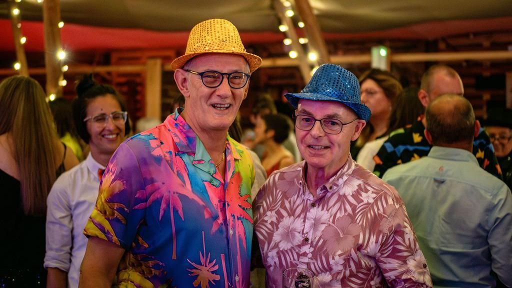 Two older men in floral shirts and colourful hats