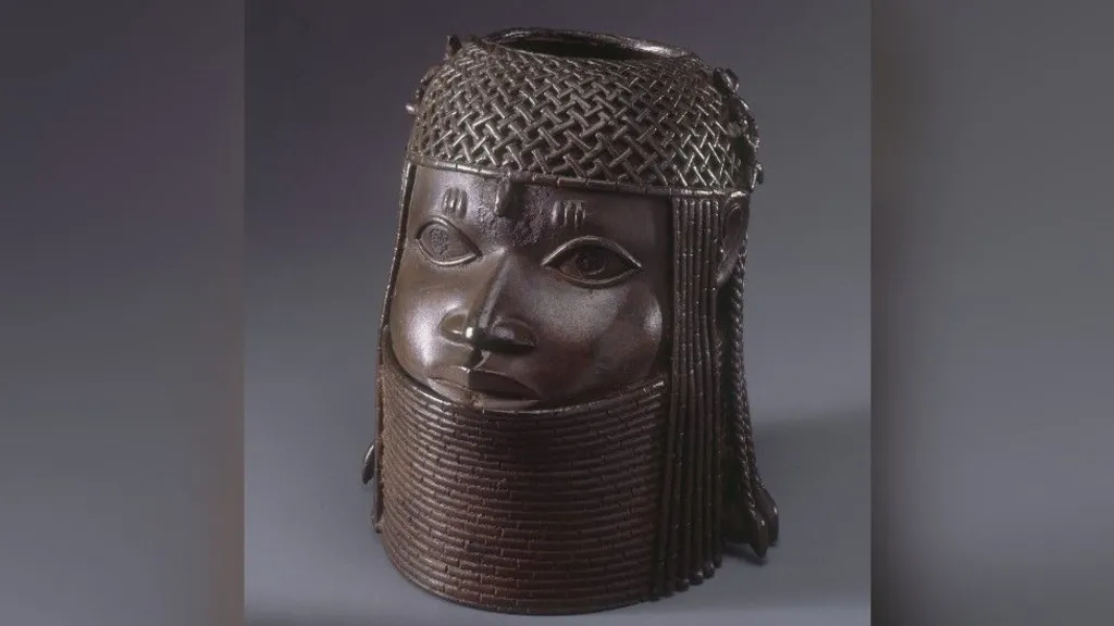 Commemorative head of the Oba, or king. It is a dark brown metal sculpture showing a face with a chain-mail helmet on its head and a metal collar up to its chin.