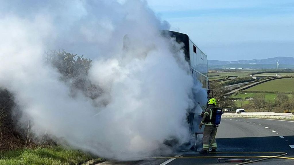 A firefighter extinguishes a bus fire on the A30 near Bodmin