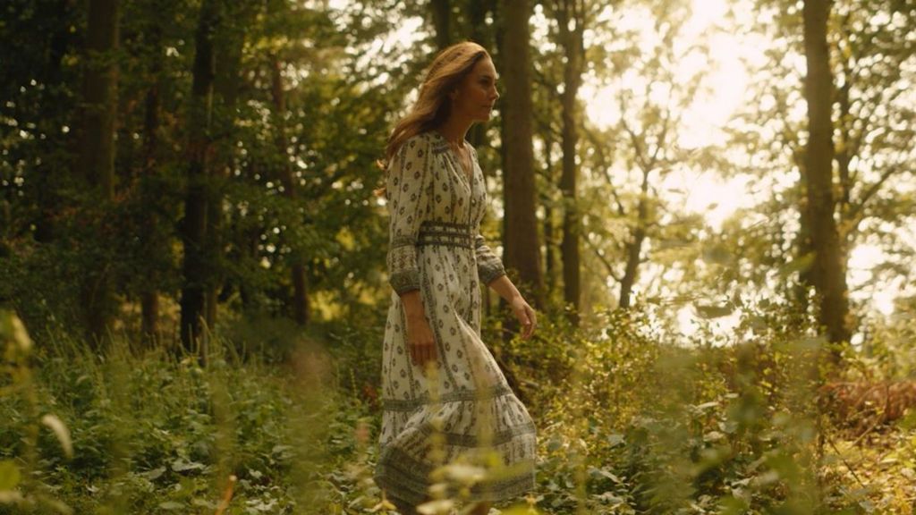 The Princess of Wales walks purposefully wearing a white and blue summer dress through a forest scene in the video message