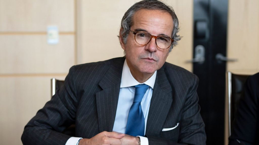 The director general of the International Atomic Energy Agency (IAEA), Rafael Grossi in a blck suit and blue tie against a beige background, lheis looking at the camera and wearing glasses
