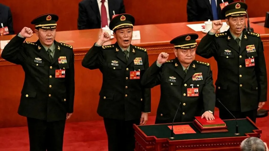 Four high-ranking Chinese military leaders hold raised right fists as they stand on pristine red carpet and swear oaths in a large formal meeting of communist party officials.