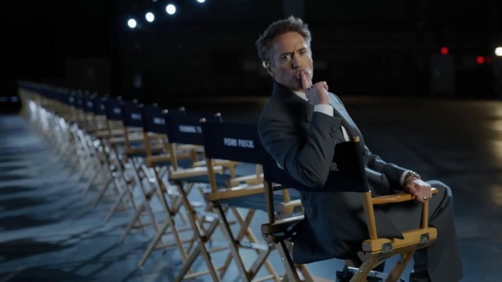 Robert Downey Junior sitting in a chair in a film studio with his finger over his mouth indicating 'shush'