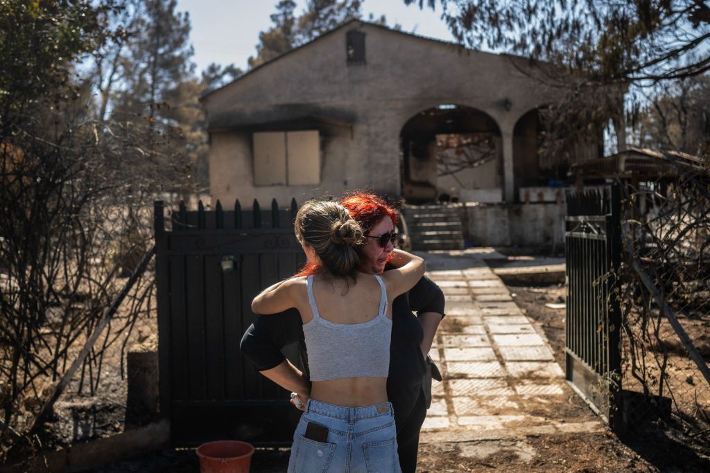 Relatives comfort each other after looking at the damage to their burnt home following a wildfire 