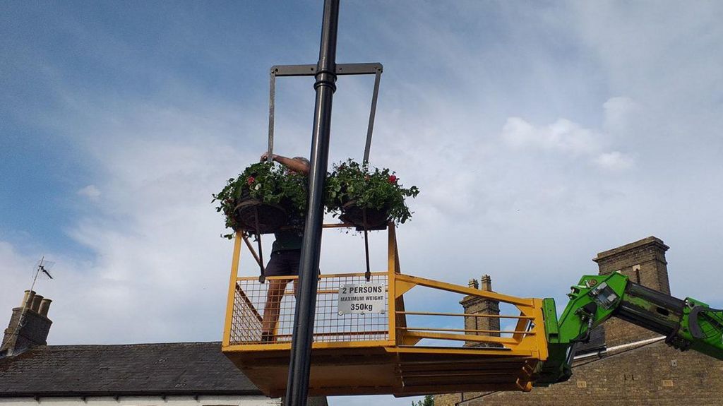 A man putting hanging baskets on a lamppost 