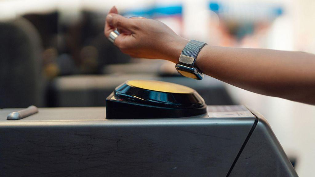 A person scans their smartwatch on a train gate.