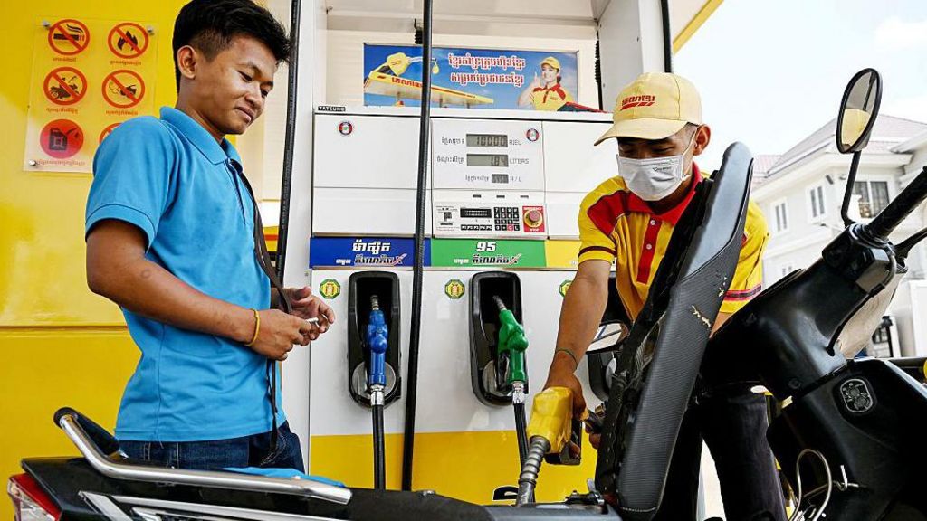 An employee pumps fuel into a motorbike as a customer his right watches
