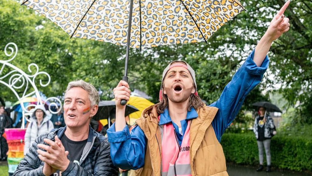 Two people applaud beneath an umbrella