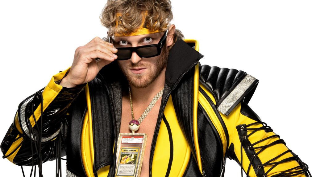 Logan Paul with an elaborate yellow and black jacket, yellow headband and sunglasses which he is pulling down to show his eyes, and the Pokemon card in a jewelled clear case hanging around his neck on a chunky gold chain